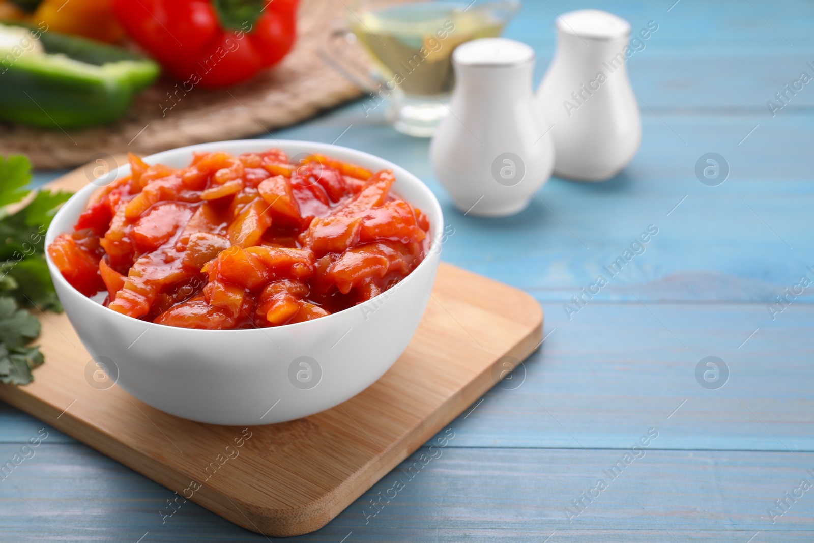 Photo of Bowl of delicious lecho on light blue wooden table, closeup. Space for text