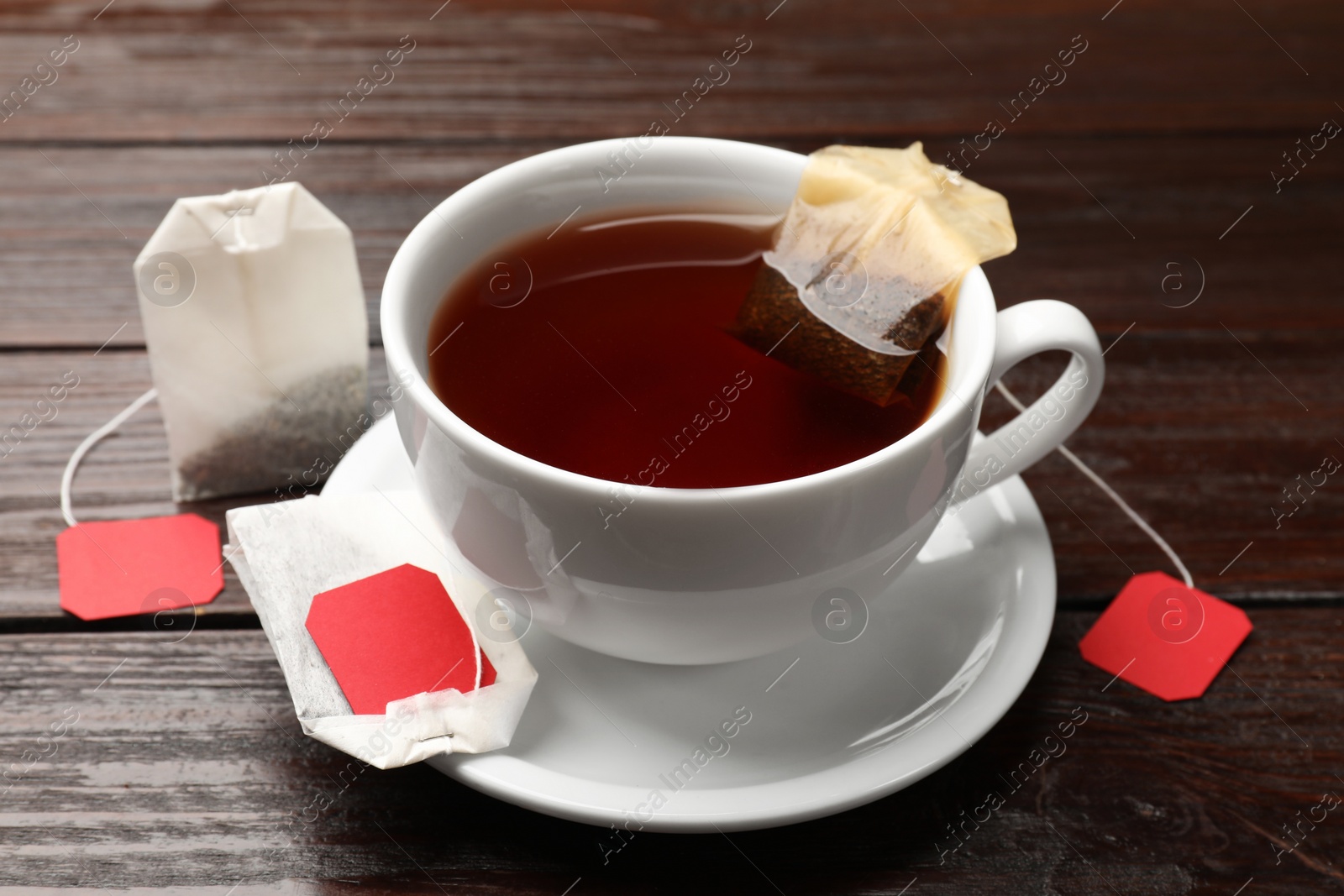 Photo of Tea bags and cup of hot beverage on wooden table, closeup