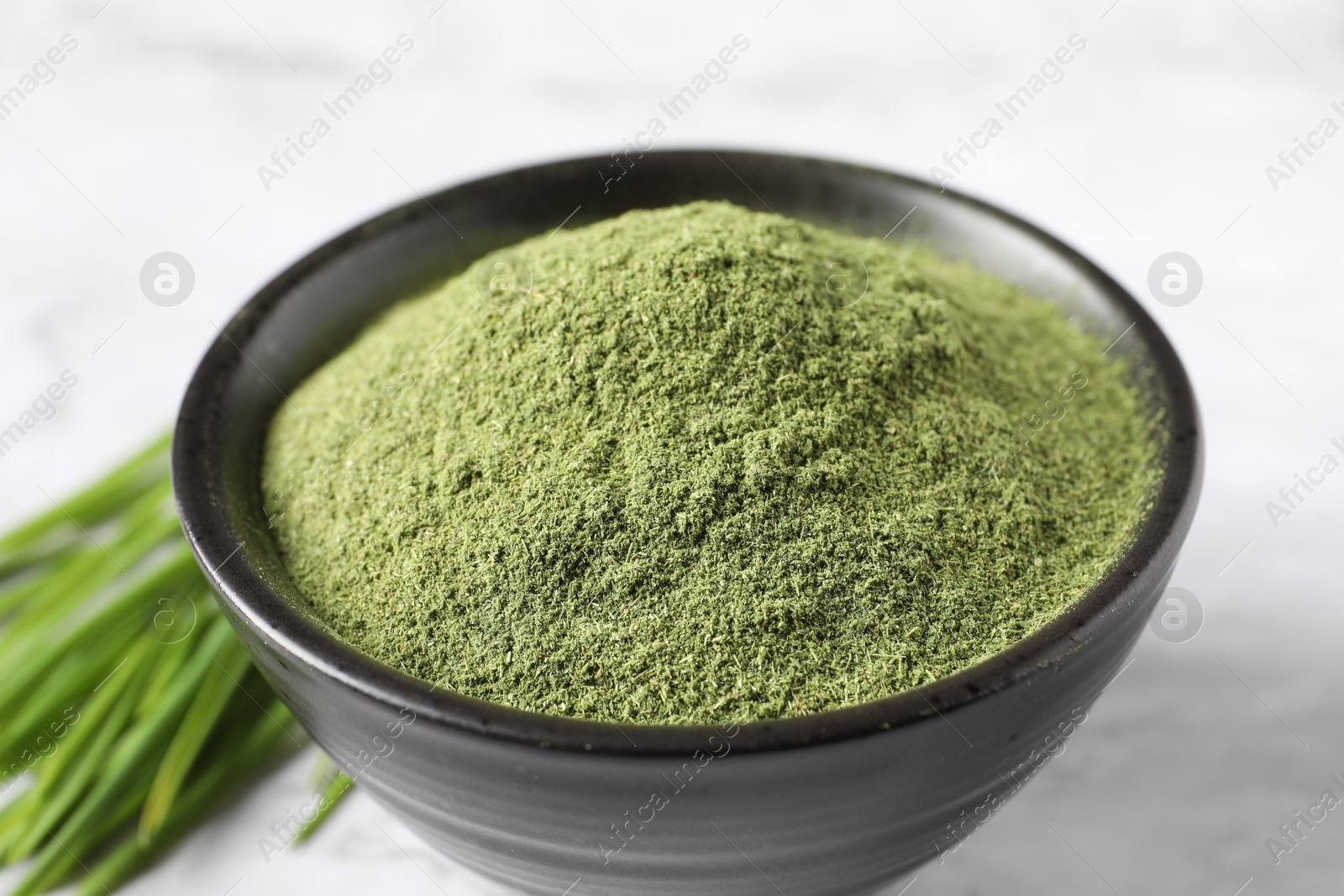 Photo of Wheat grass powder in bowl on white table, closeup