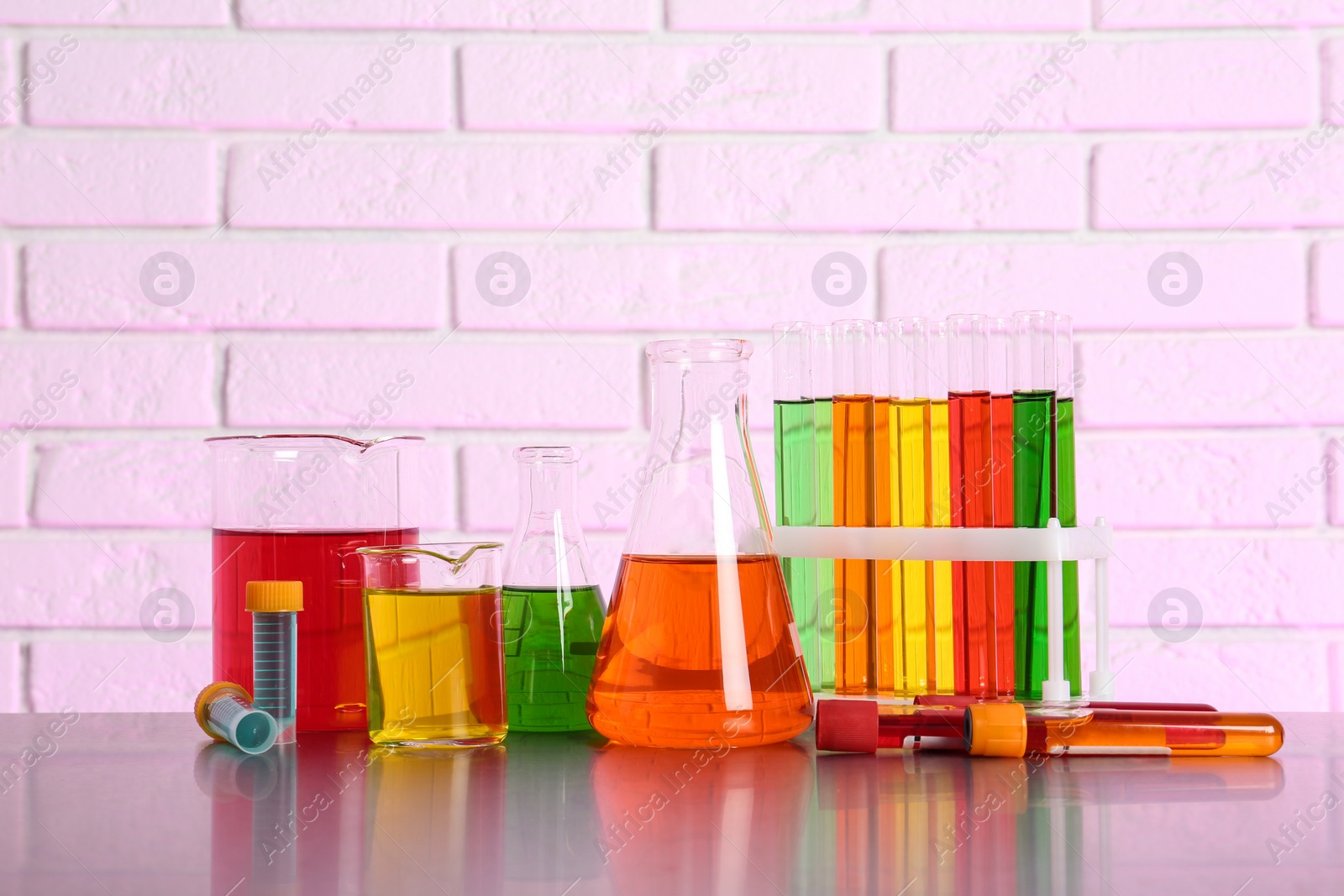 Photo of Different glassware with samples on table near brick wall. Solution chemistry