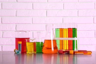 Different glassware with samples on table near brick wall. Solution chemistry