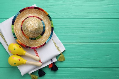 Photo of Mexican sombrero hat, maracas and poncho on turquoise wooden table, flat lay. Space for text