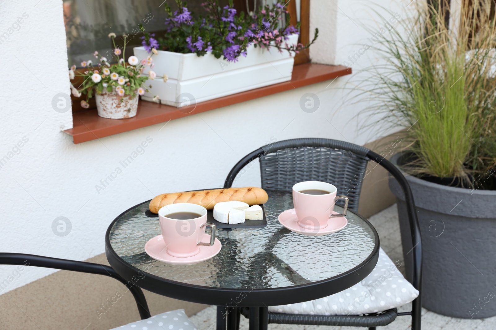 Photo of Cups of coffee, bread and cheese on glass table. Relaxing place at outdoor terrace