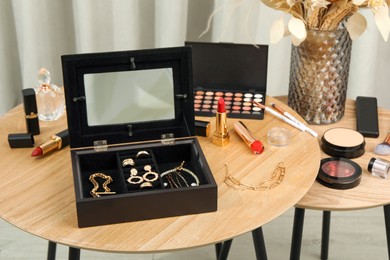 Photo of Jewelry box with stylish golden bijouterie and makeup products on wooden table indoors