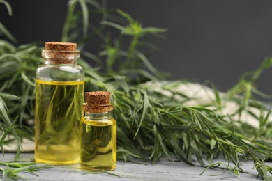 Bottles of essential oil and fresh tarragon leaves on grey wooden table. Space for text