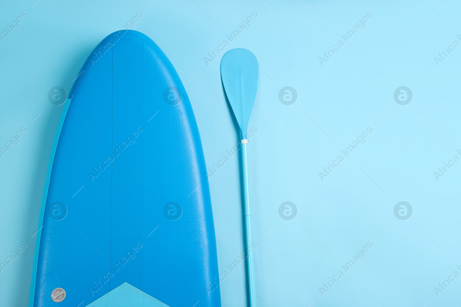 Photo of Board and paddle for standup paddleboarding (SUP) on light blue background, flat lay. Space for text