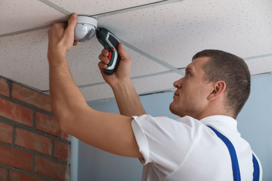 Technician installing CCTV camera on ceiling indoors