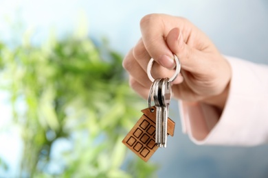 Photo of Woman holding house keys with trinket on blurred background, closeup. Space for text