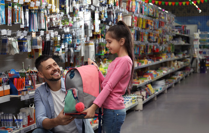 Little girl with father choosing school stationery in supermarket