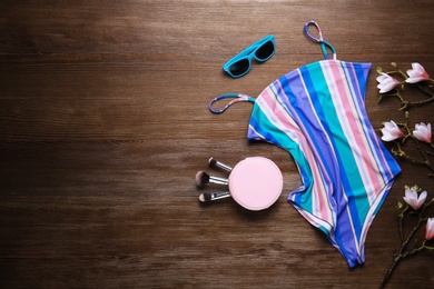Photo of Beautiful swimsuit, sunglasses and cosmetic bag with brushes on wooden background, top view