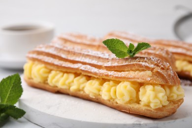 Photo of Delicious eclairs filled with cream and mint on table, closeup