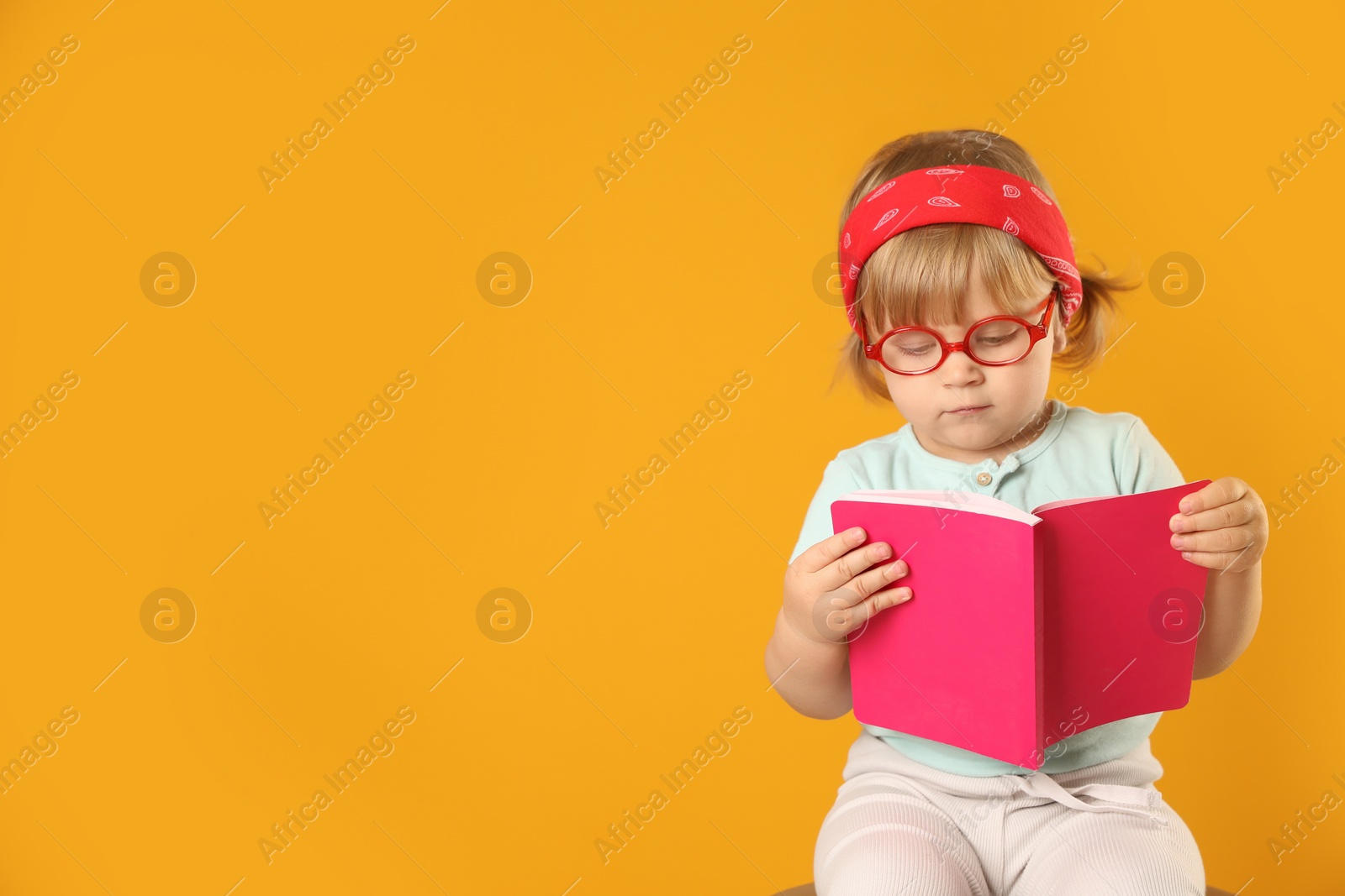 Photo of Cute little girl in glasses with notebook on orange background. Space for text