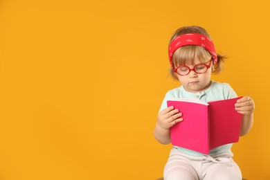 Cute little girl in glasses with notebook on orange background. Space for text