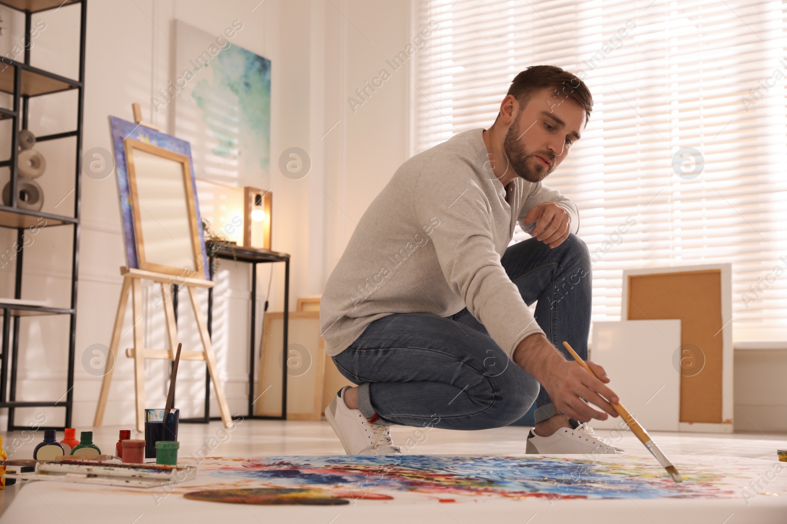 Photo of Young man painting on canvas with brush in artist studio