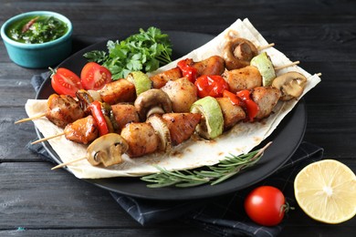 Photo of Delicious shish kebabs with vegetables served on black wooden table, closeup
