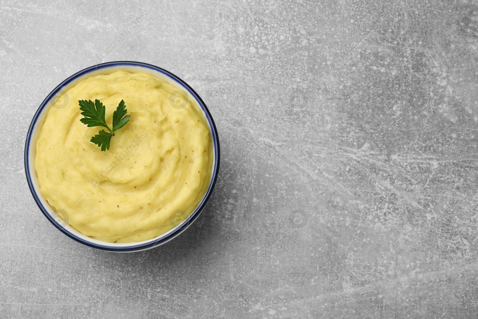 Photo of Bowl of tasty mashed potatoes with parsley on grey marble table, top view. Space for text