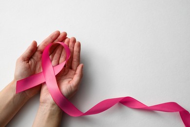 Photo of Woman holding pink ribbon on white background, top view with space for text. Breast cancer awareness concept