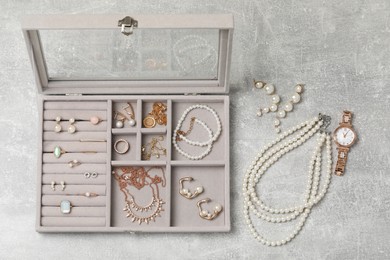 Photo of Jewelry box with many different accessories on light grey table, flat lay