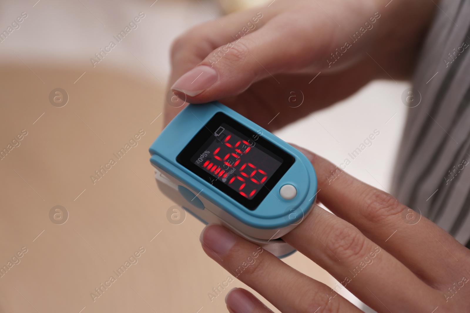 Photo of Woman measuring oxygen level with modern fingertip pulse oximeter indoors, closeup