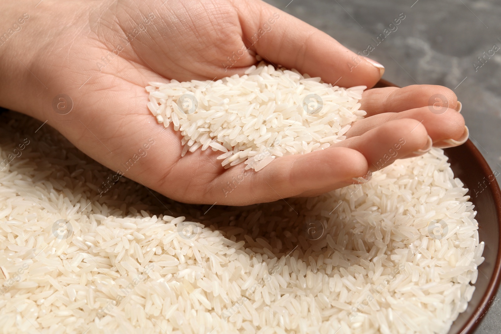 Photo of Woman holding grains near plate with rice on table, closeup