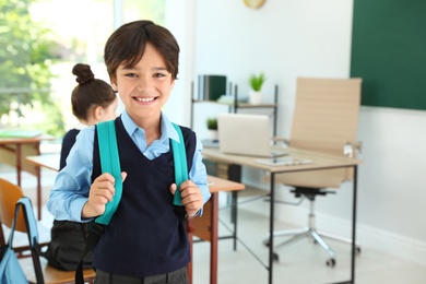 Boy wearing school uniform with backpack in classroom