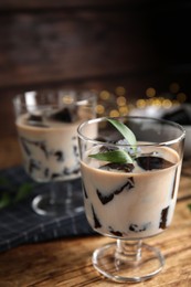 Photo of Glass of milk with grass jelly and green leaves on wooden table, closeup