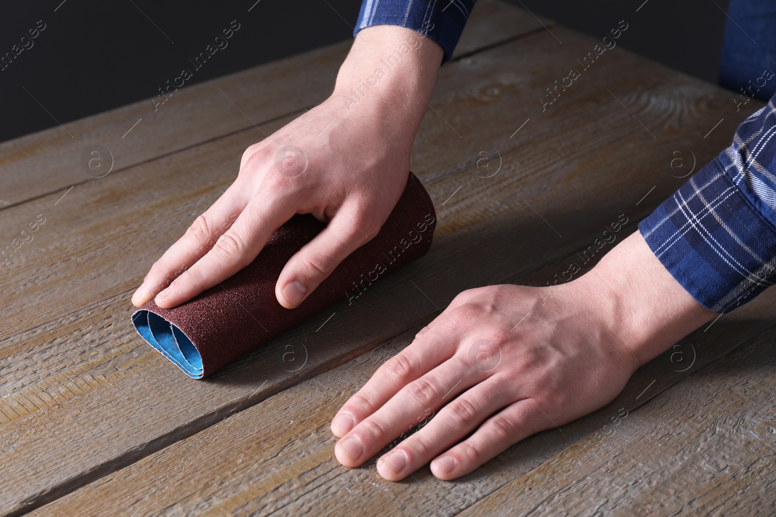 Photo of Man polishing wooden table with rolled sheet of sandpaper, closeup