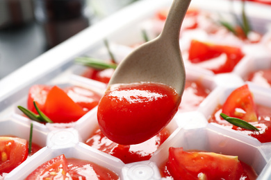 Pouring sauce into ice cube tray with tomatoes and rosemary, closeup
