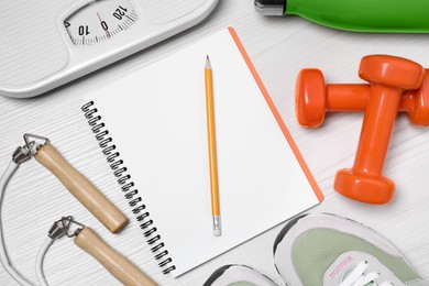 Notebook, scales and sports equipment on white wooden table, flat lay. Personal training