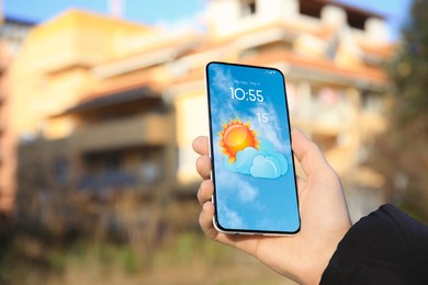 Woman checking weather using app on smartphone outdoors, closeup. Data and illustration of sun with cloud on screen