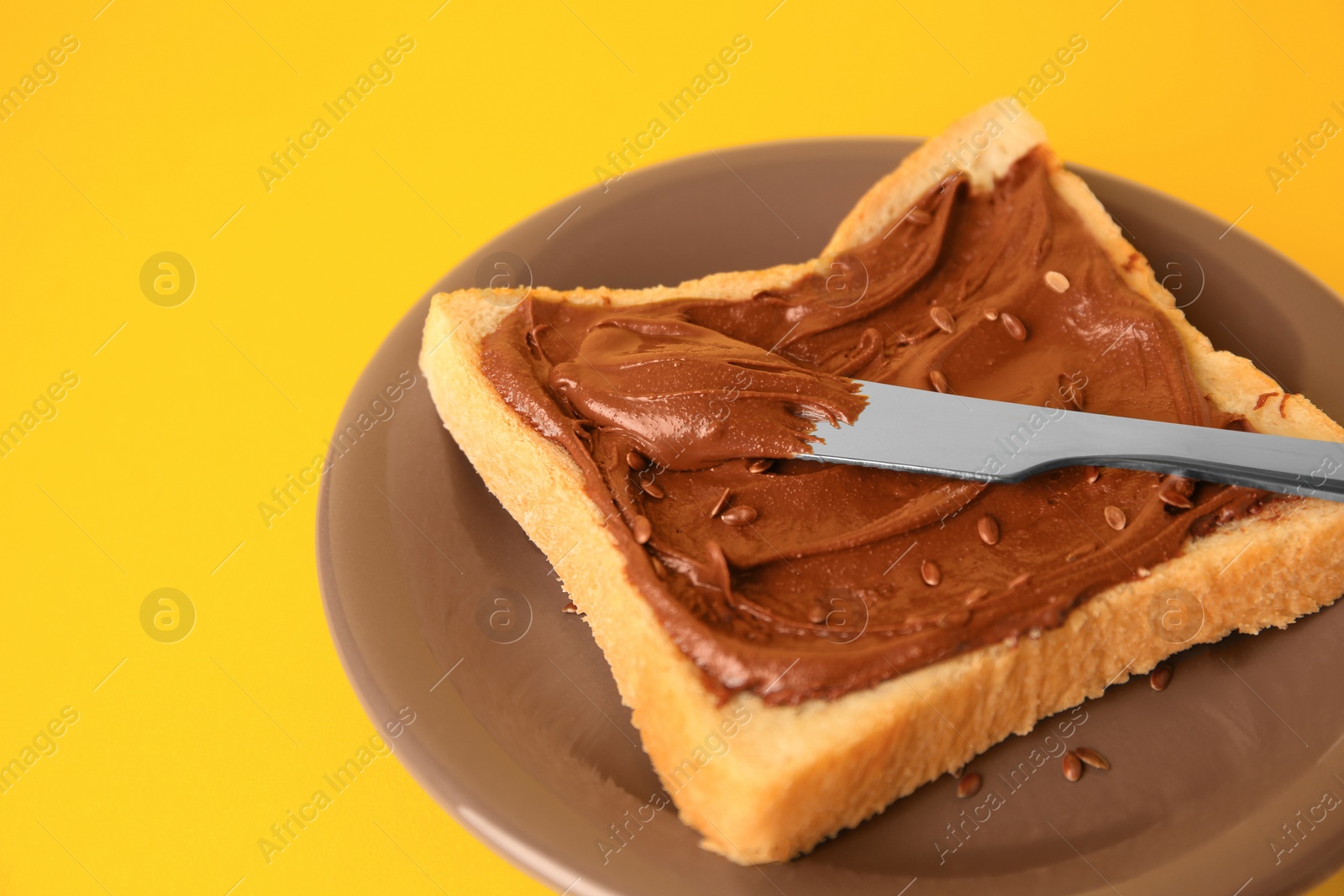 Photo of Spreading chocolate paste onto bread on yellow background, closeup. Space for text