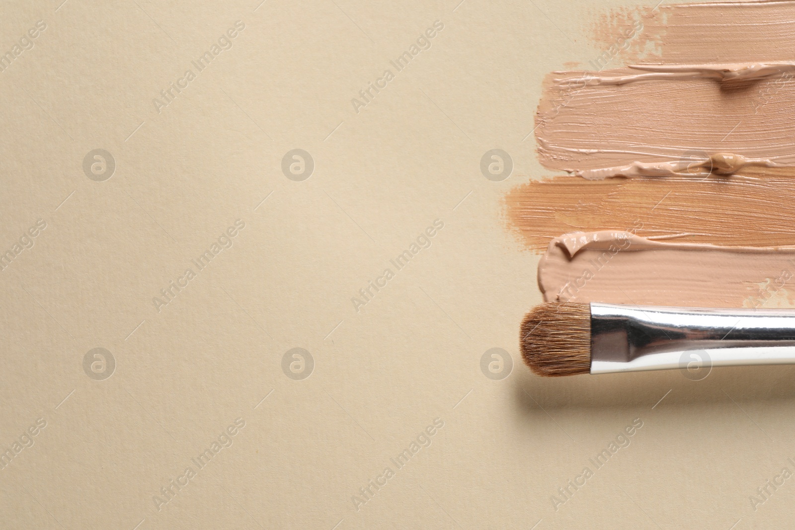 Photo of Samples of skin foundation and makeup brush on beige background, top view. Space for text