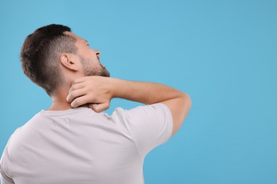 Photo of Allergy symptom. Man scratching his neck on light blue background. Space for text