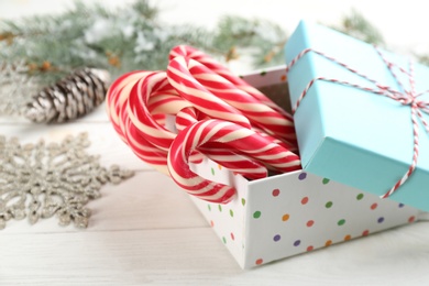 Many sweet candy canes in gift box on white wooden table, closeup. Traditional Christmas treat