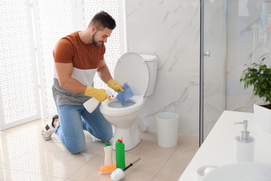 Photo of Young man cleaning toilet bowl in bathroom