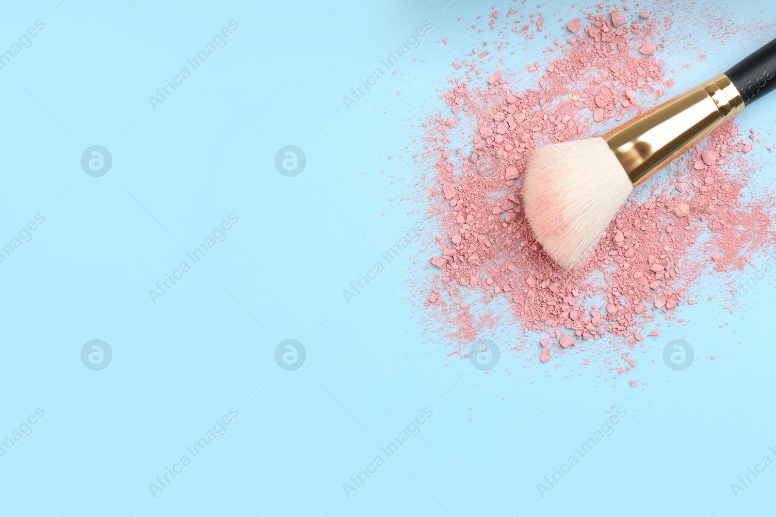 Photo of Makeup brush and scattered blush on light blue background, top view. Space for text