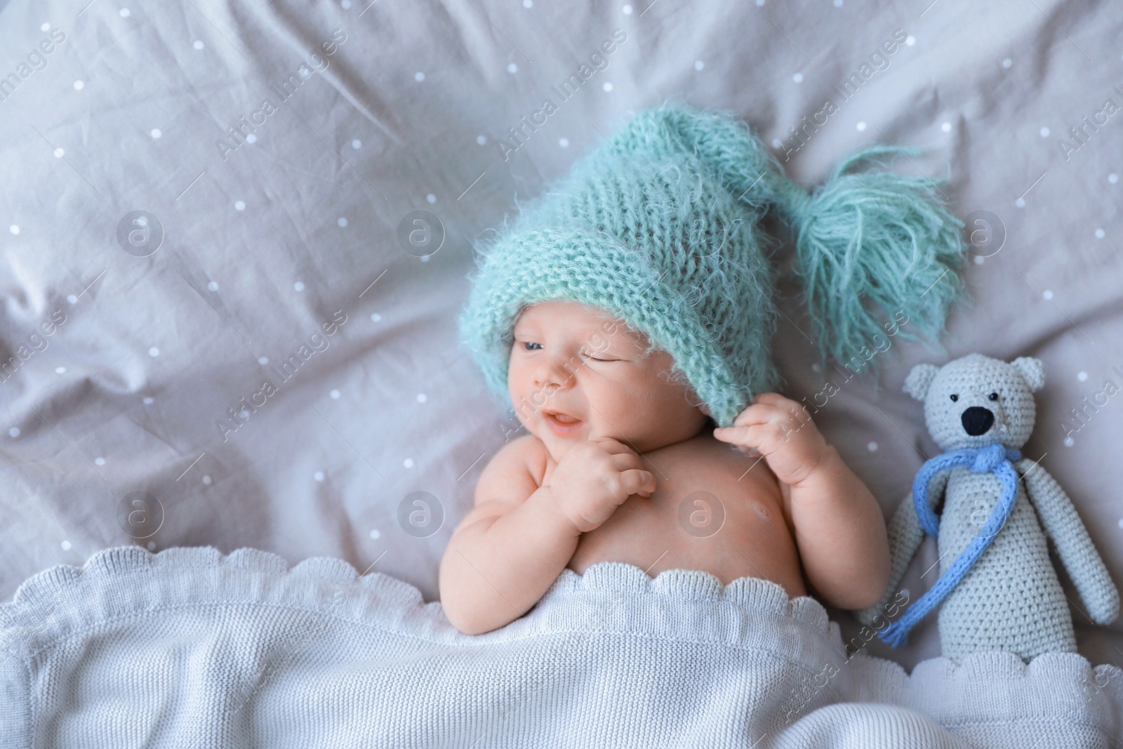 Photo of Cute newborn baby in warm hat with toy lying on bed, top view