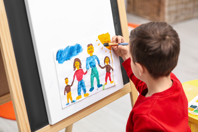 Little child painting on easel in room