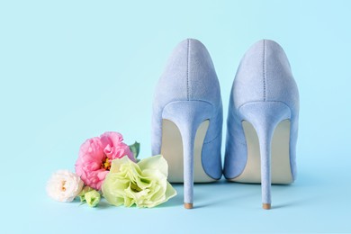 Photo of Stylish women's high heeled shoes and beautiful flowers on light blue background