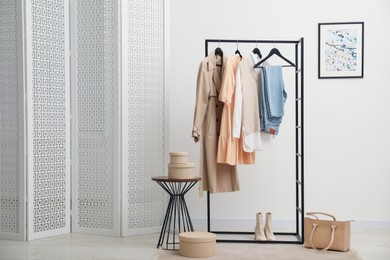 Rack with different stylish women's clothes, boots, bag and side table indoors