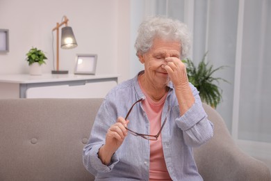 Senior woman with headache sitting on sofa at home. Space for text