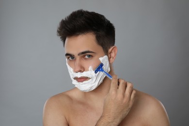 Photo of Handsome young man shaving with razor on grey background