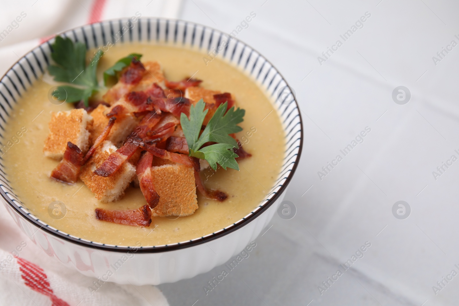 Photo of Delicious lentil soup with bacon and parsley in bowl on white tiled table, closeup