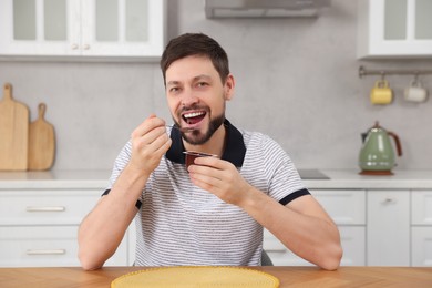 Photo of Handsome man eating tasty yogurt at table in kitchen