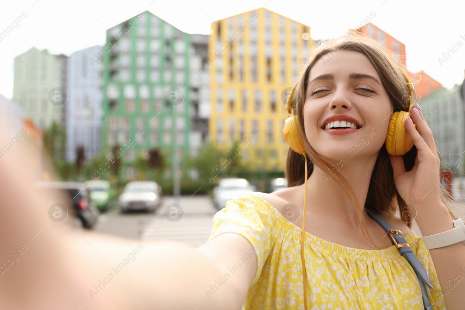 Photo of Beautiful young woman taking selfie while listening to music with headphones on sunny day outdoors