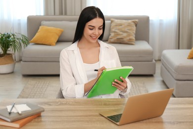 Photo of Young woman taking notes during online webinar at table indoors