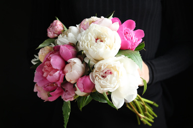 Woman with bouquet of beautiful peonies on black background, closeup