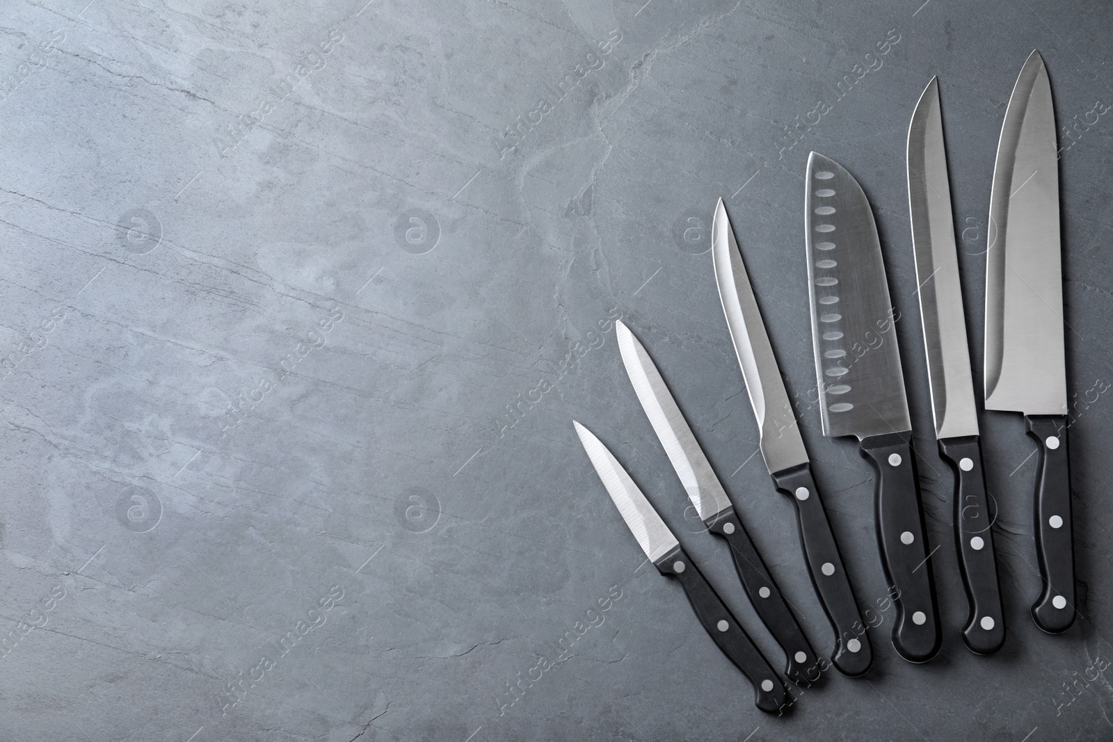 Photo of Set of sharp kitchen knives on stone surface, top view with space for text