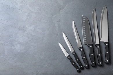 Photo of Set of sharp kitchen knives on stone surface, top view with space for text