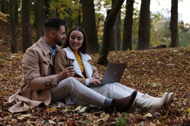 Happy young couple with laptop spending time together in autumn park